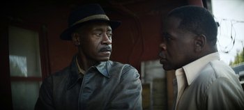 Movie still from “No Sudden Move” (2021), directed by Steven Soderbergh – A man wearing a hat talking to another man; Close Up shot, Over the shoulder angle