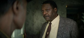 Movie still from “No Sudden Move” (2021), directed by Steven Soderbergh – A man wearing a suit and tie looking at the camera; Close Up shot, Over the shoulder angle