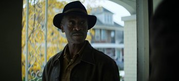 Movie still from “No Sudden Move” (2021), directed by Steven Soderbergh – A man wearing a black hat and a brown jacket; Close Up shot, Over the shoulder angle