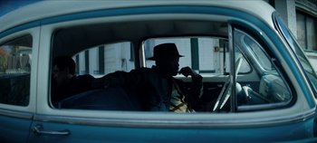Movie still from “No Sudden Move” (2021), directed by Steven Soderbergh – A man sitting in the back seat of a blue car; Medium shot, Low angle