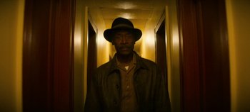 Movie still from “No Sudden Move” (2021), directed by Steven Soderbergh – A man wearing a hat standing in a hallway; Medium shot, Low angle