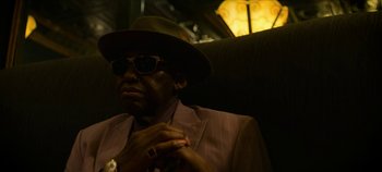 Movie still from “No Sudden Move” (2021), directed by Steven Soderbergh – A man sitting on top of a chair wearing a hat; Close Up shot, Low angle