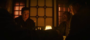 Movie still from “No Sudden Move” (2021), directed by Steven Soderbergh – Two men sitting at a table in a dimly - lit room; Medium shot, Over the shoulder angle