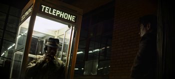 Movie still from “No Sudden Move” (2021), directed by Steven Soderbergh – A man in a hat is talking on a phone; Medium shot, Low angle