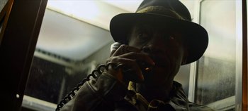 Movie still from “No Sudden Move” (2021), directed by Steven Soderbergh – A man wearing a fedora talking on a phone; Close Up shot, Low angle