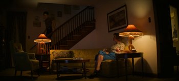 Movie still from “No Sudden Move” (2021), directed by Steven Soderbergh – A woman sitting on a couch in a living room; Wide shot, Low angle