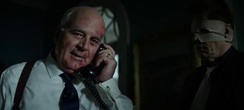 Movie still from “No Sudden Move” (2021), directed by Steven Soderbergh – An older man talking on a phone in a dark room; Close Up shot, Low angle