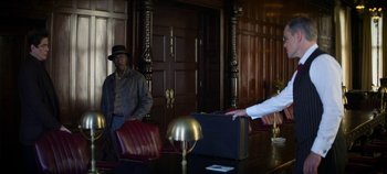 Movie still from “No Sudden Move” (2021), directed by Steven Soderbergh – A man in a hat is holding a suit case in front of a man in a hat; Medium shot, Over the shoulder angle