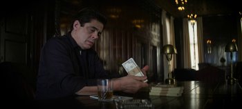 Movie still from “No Sudden Move” (2021), directed by Steven Soderbergh – A man sitting at a table with a stack of books in front of him; Medium shot, Low angle