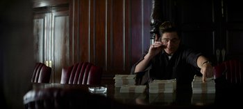 Movie still from “No Sudden Move” (2021), directed by Steven Soderbergh – A person sitting at a table talking on a cell phone; Medium shot, Over the shoulder angle