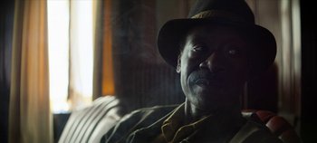 Movie still from “No Sudden Move” (2021), directed by Steven Soderbergh – A person wearing a hat on a couch; Close Up shot, Low angle