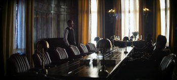 Movie still from “No Sudden Move” (2021), directed by Steven Soderbergh – A man standing in front of a long wooden table; Wide shot, Over the shoulder angle