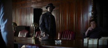 Movie still from “No Sudden Move” (2021), directed by Steven Soderbergh – A man standing at a wooden table in a room; Medium shot, Low angle