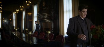 Movie still from “No Sudden Move” (2021), directed by Steven Soderbergh – A man in a suit sitting at a table in front of a fire place; Medium shot, Low angle