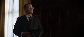 Movie still from “No Sudden Move” (2021), directed by Steven Soderbergh – A man in a suit and tie holding a black hat; Medium shot, Low angle