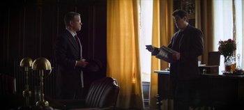 Movie still from “No Sudden Move” (2021), directed by Steven Soderbergh – A man in a suit and tie standing in front of a window; Medium shot, Over the shoulder angle