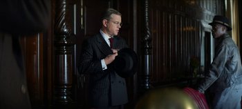 Movie still from “No Sudden Move” (2021), directed by Steven Soderbergh – A man in a suit and tie holding a hat; Medium shot, Over the shoulder angle