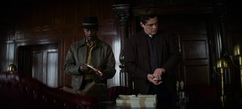 Movie still from “No Sudden Move” (2021), directed by Steven Soderbergh – Two men standing next to each other in front of a table; Medium shot, Low angle