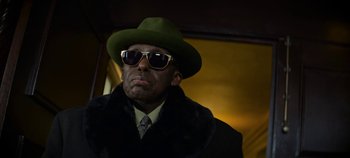 Movie still from “No Sudden Move” (2021), directed by Steven Soderbergh – A man wearing a green hat and sunglasses; Close Up shot, Low angle