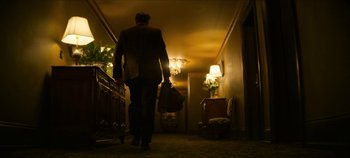 Movie still from “No Sudden Move” (2021), directed by Steven Soderbergh – A man walking down a hallway holding a bag of luggage; Wide shot, Low angle