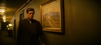 Movie still from “No Sudden Move” (2021), directed by Steven Soderbergh – A man standing in front of a painting in a room; Medium shot, Low angle