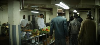 Movie still from “No Sudden Move” (2021), directed by Steven Soderbergh – A group of people standing in a kitchen preparing food; Wide shot, Over the shoulder angle