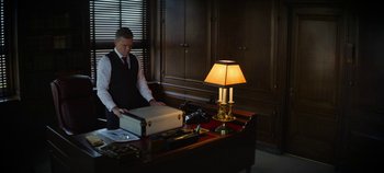 Movie still from “No Sudden Move” (2021), directed by Steven Soderbergh – A man sitting at a desk in a room; Medium shot, High angle