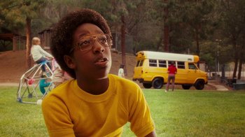 Movie still from “Norbit” (2007), directed by Brian Robbins – A young man sitting in a field with a yellow van in the background; Close Up shot, Low angle