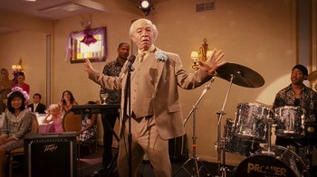 Movie still from “Norbit” (2007), directed by Brian Robbins – An older man in a brown suit is singing into a microphone; Medium shot, Low angle