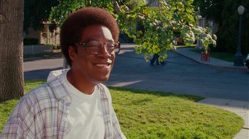 Movie still from “Norbit” (2007), directed by Brian Robbins – A young man with glasses smiling for the camera; Medium shot, Over the shoulder angle