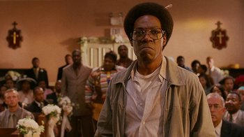 Movie still from “Norbit” (2007), directed by Brian Robbins – A man in a brown jacket and glasses is standing in front of a group of people; Close Up shot, Low angle