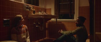 Movie still from “Mother/Android” (2021), directed by Mattson Tomlin – A man sitting on the floor of a bathroom next to a sink; Wide shot, High angle