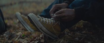 Movie still from “Mother/Android” (2021), directed by Mattson Tomlin – A person tying their shoe on the ground in the woods; Extreme Close Up shot, High angle