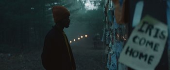 Movie still from “Mother/Android” (2021), directed by Mattson Tomlin – A man standing in the dark looking at a wall of papers; Medium shot, Over the shoulder angle