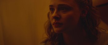 Movie still from “Mother/Android” (2021), directed by Mattson Tomlin – A young woman looking into the distance in a dimly - lit room; Close Up shot, Over the shoulder angle
