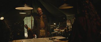 Movie still from “Mother/Android” (2021), directed by Mattson Tomlin – An older man standing in front of a table; Medium shot, Over the shoulder angle