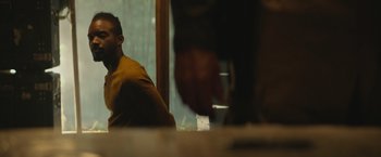 Movie still from “Mother/Android” (2021), directed by Mattson Tomlin – A man sitting at a table with a glass of water; Medium shot, Over the shoulder angle