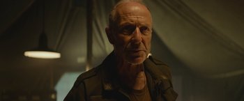 Movie still from “Mother/Android” (2021), directed by Mattson Tomlin – An older man wearing a jacket and a necklace; Close Up shot, Low angle