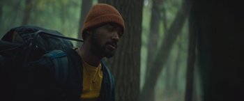 Movie still from “Mother/Android” (2021), directed by Mattson Tomlin – A man wearing a hat sitting in the woods; Close Up shot, Low angle