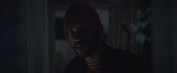 Movie still from “Mother/Android” (2021), directed by Mattson Tomlin – A man wearing a red hat in a dark room; Close Up shot, Low angle