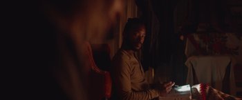 Movie still from “Mother/Android” (2021), directed by Mattson Tomlin – A man sitting at a table in a dark room; Medium shot, Over the shoulder angle