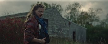 Movie still from “Mother/Android” (2021), directed by Mattson Tomlin – A woman in a plaid shirt is standing in front of an old barn; Medium shot, Over the shoulder angle