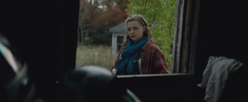 Movie still from “Mother/Android” (2021), directed by Mattson Tomlin – A woman in a plaid shirt and a blue scarf looking into a mirror; Medium shot, Over the shoulder angle