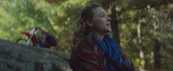 Movie still from “Mother/Android” (2021), directed by Mattson Tomlin – A young woman with long blonde curly hair wearing a red and blue jacket; Close Up shot, Over the shoulder angle