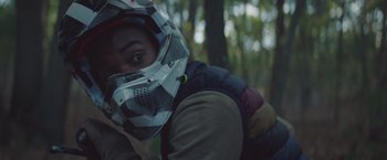 Movie still from “Mother/Android” (2021), directed by Mattson Tomlin – A person wearing a helmet in the woods; Close Up shot, Over the shoulder angle