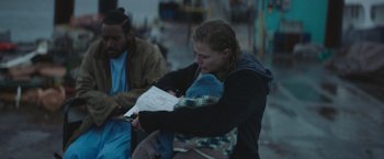 Movie still from “Mother/Android” (2021), directed by Mattson Tomlin – A woman holding a baby and looking at a piece of paper; Medium shot, Over the shoulder angle