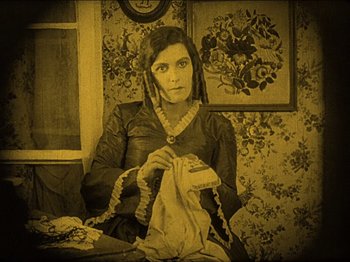 Movie still from “Nosferatu” (1922), directed by F.W. Murnau – A woman sitting at a table holding a piece of cloth; Medium shot, High angle