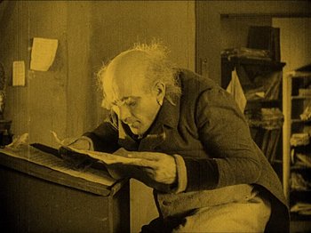 Movie still from “Nosferatu” (1922), directed by F.W. Murnau – An old man reading a newspaper in a room with yellow walls; Medium shot, High angle