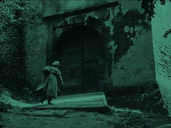 Movie still from “Nosferatu” (1922), directed by F.W. Murnau – A man in a trench coat walking towards a door; Wide shot, Low angle
