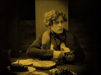 Movie still from “Nosferatu” (1922), directed by F.W. Murnau – A man sitting at a table with a plate of food in front of him; Medium shot, High angle
